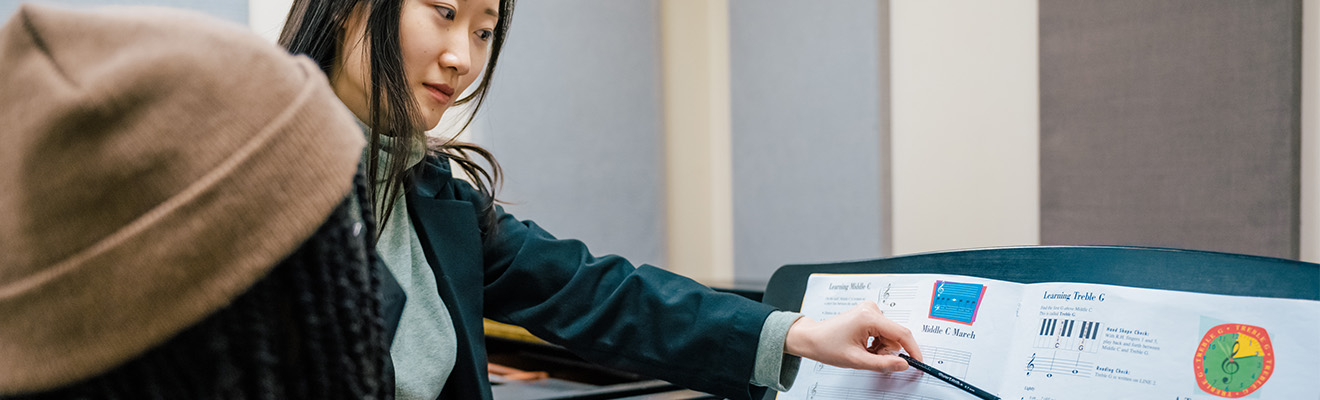 A woman points at sheet music for a piano student.