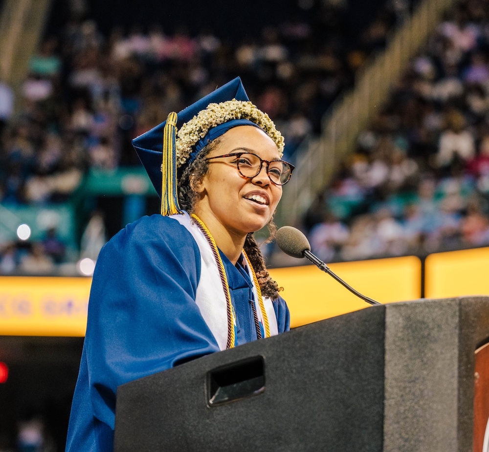 Myieh Leggette in her graduation cap and gown speaks at a podium.