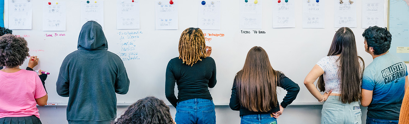 Students write Spanish on a whiteboard.