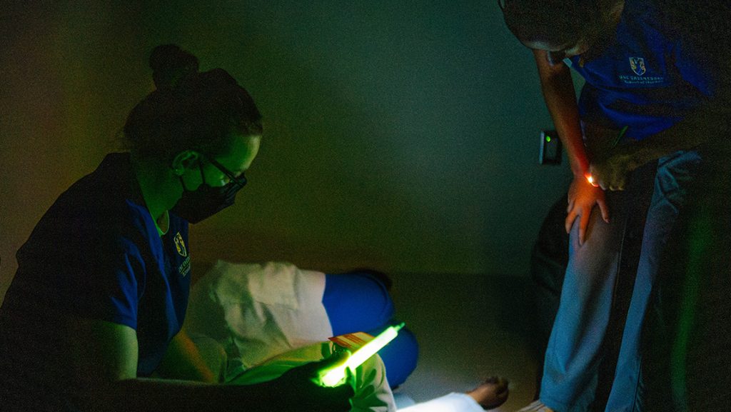 UNCG nursing students use glow sticks to see in a dark room to simulate a disaster scenario.