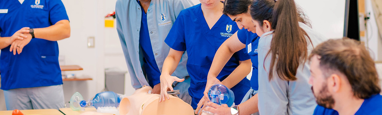 Nursing students apply a breathing apparatus to a manikin.