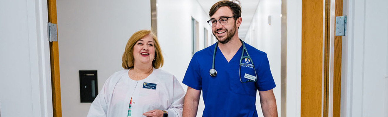 A nursing professor and student in scrubs walk down a hallway.