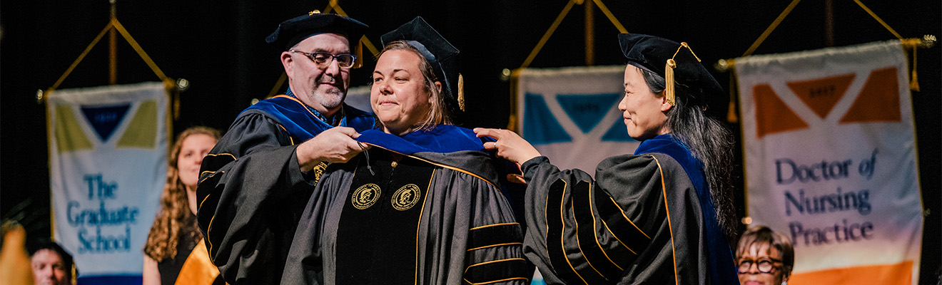 UNCG faculty place the doctoral hood over a graduate.