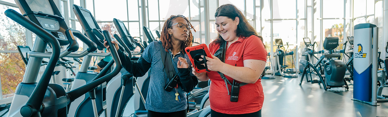A UNCG student talks to a woman in the gym.