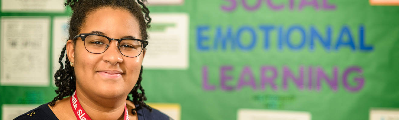 A woman standing in front a classroom display board that reads "social emotional learning."