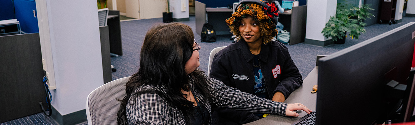 Two women sit at a library computer.