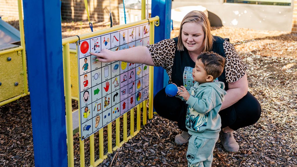 SLP Roslyn Reynolds points to the pictures on an AAC for a toddler.