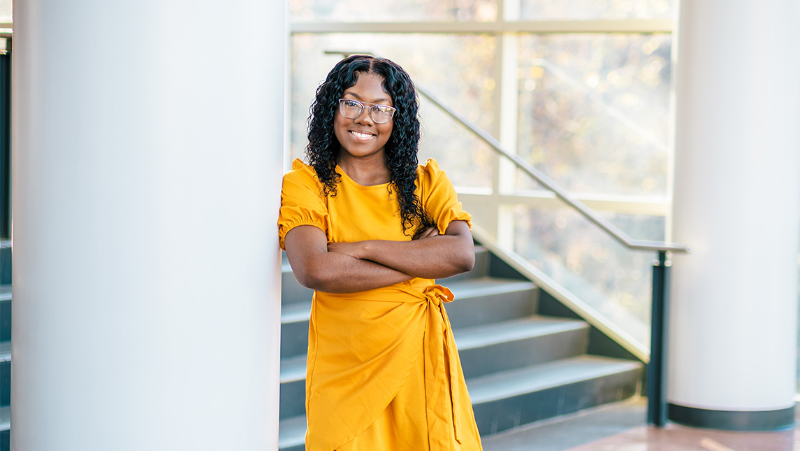 Stanysha Lowery leans against a pillar wearing a yellow dress.