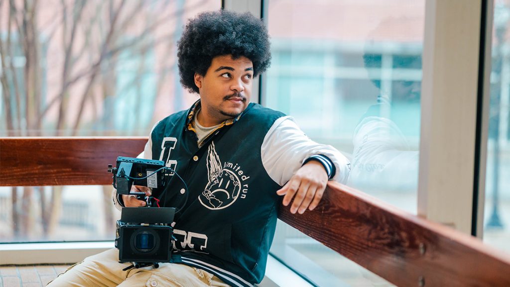 UNCG student Taylee Gaillard looks out a window while holding a video camera.