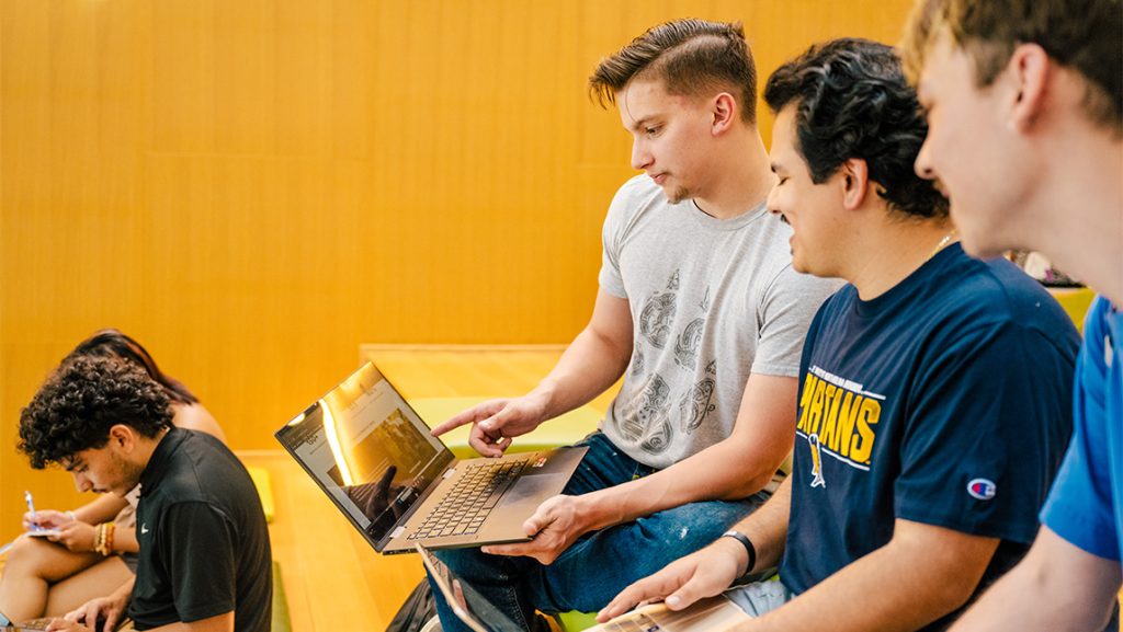 UNCG students look at a laptop together.