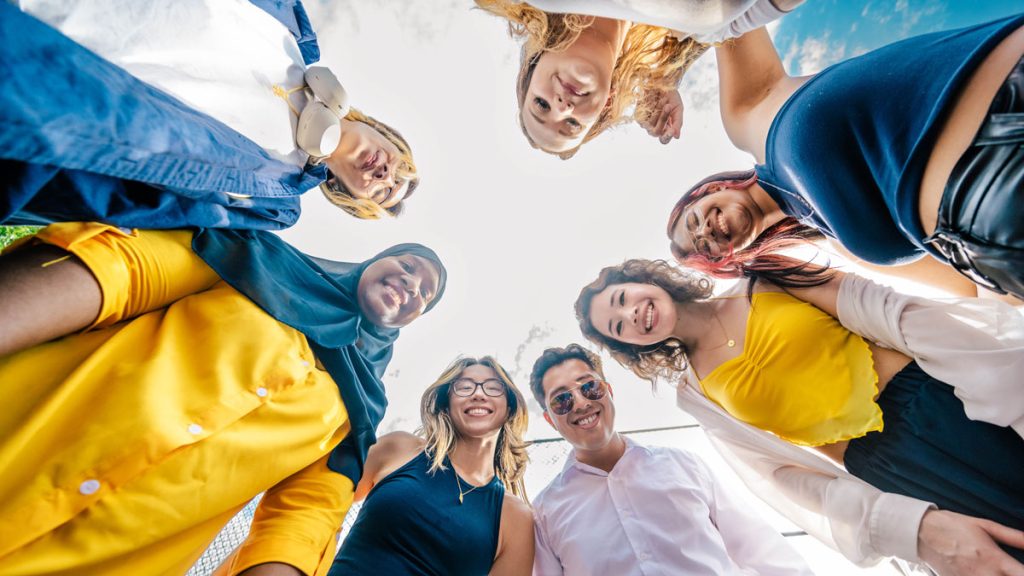 Students dressed in blue and gold huddle up and look down at the camera. 