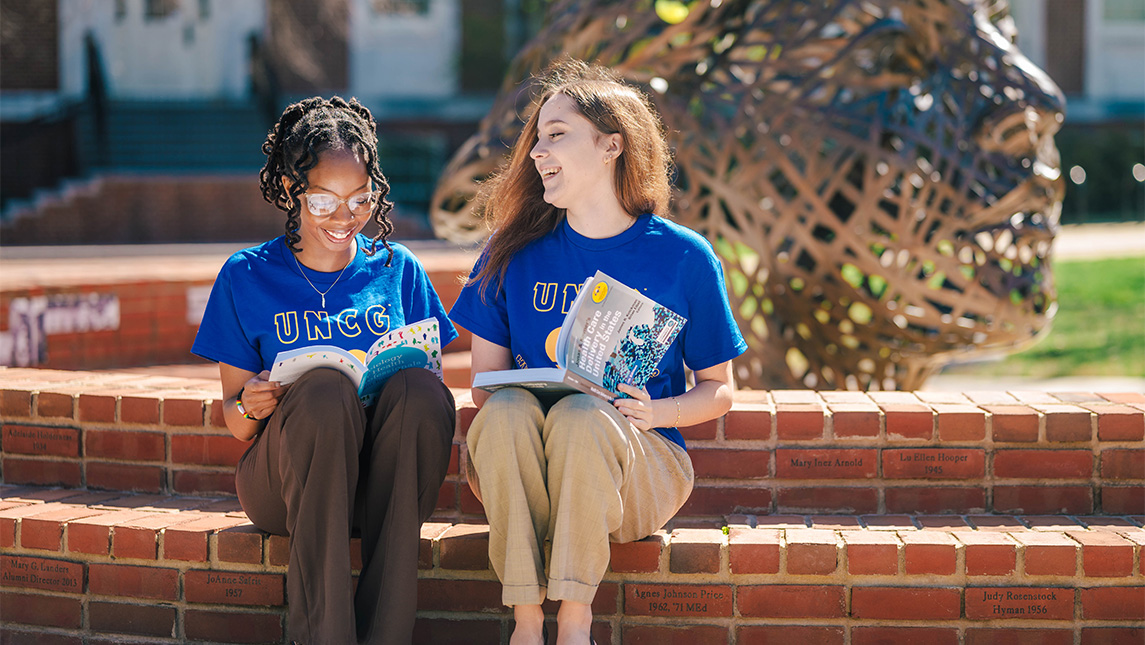 UNCG students Yawa Eklou and Mary Blake Murphy read healthcare textbooks outside.