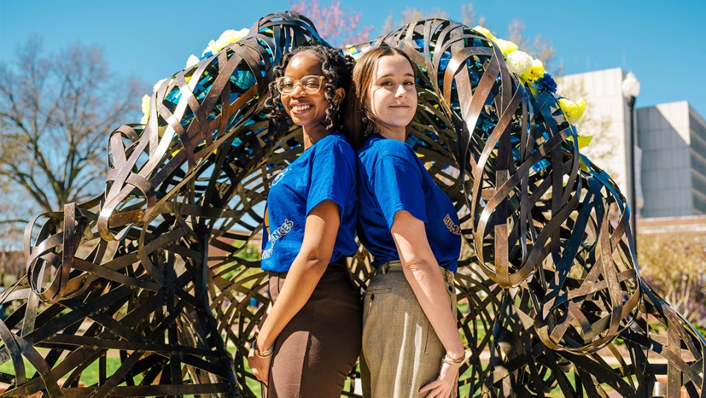 UNCG students Yawa Eklou and Mary Blake Murphy pose beside a statue.
