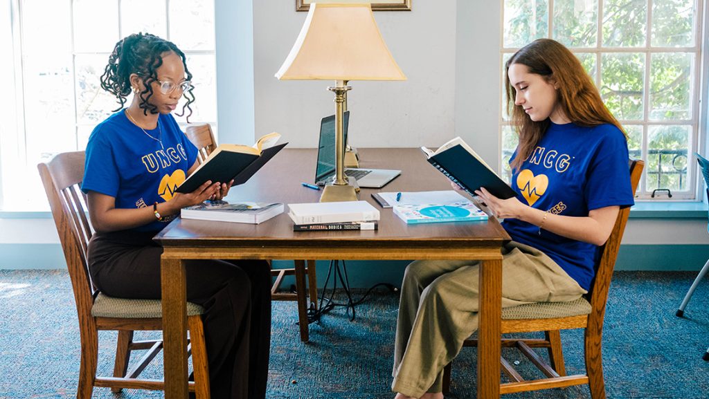 UNCG students Yawa Eklou and Mary Blake Murphy read in the library.