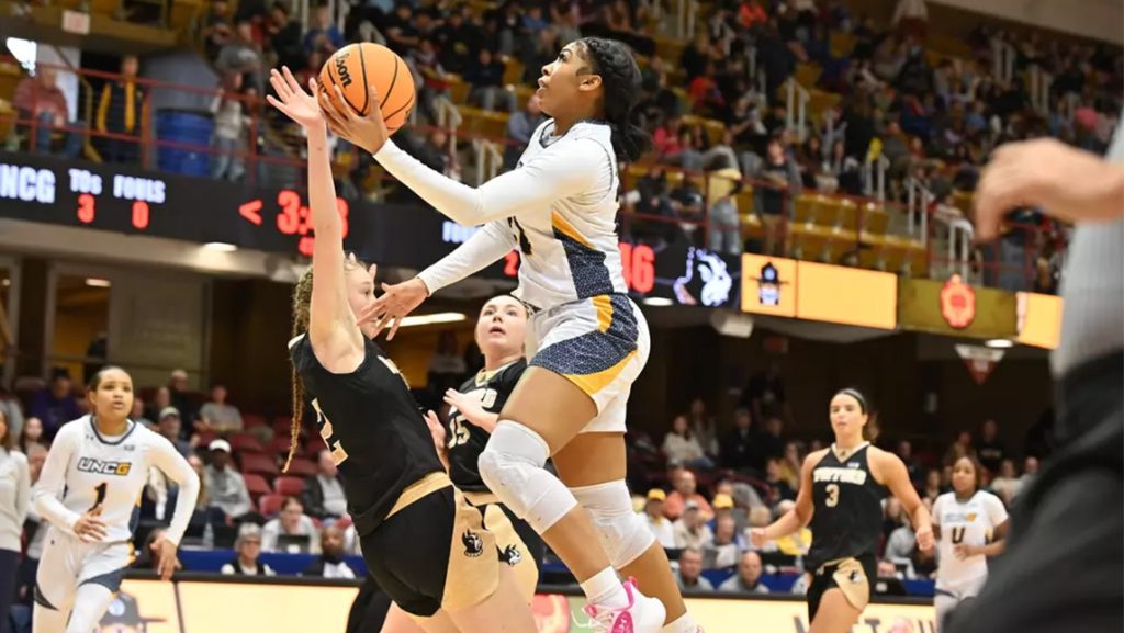 UNCG women's basketball player leaps as Wofford opponent tries to block.
