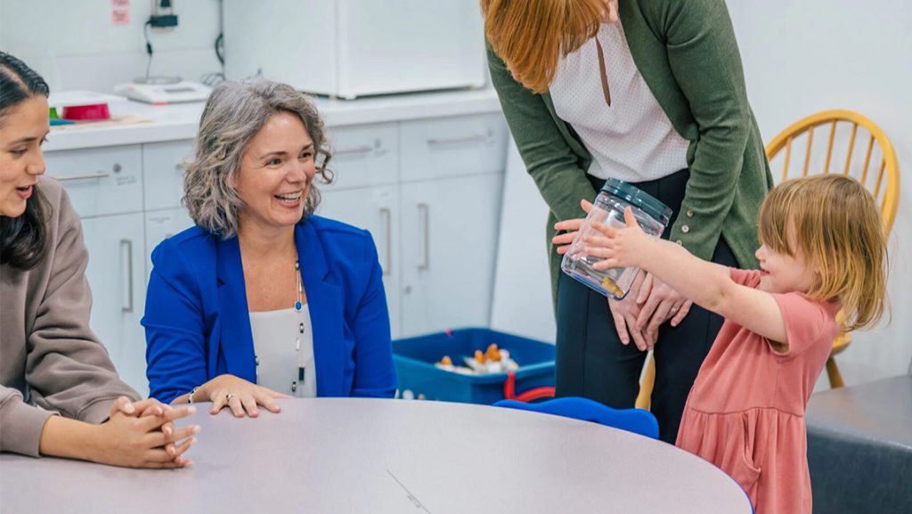 A toddler holds up a plastic jar for UNCG's Dr. Esther Leerkes.