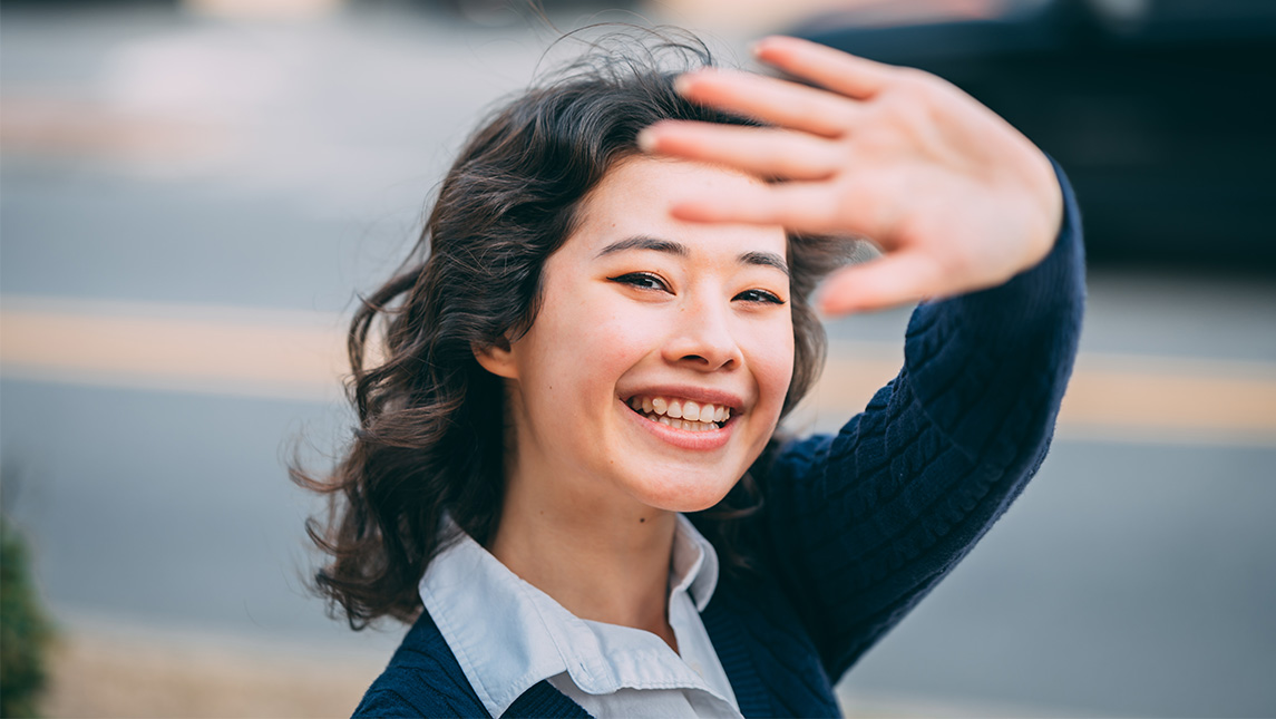 Close up of a young woman as she looks over her shoulder and waves.