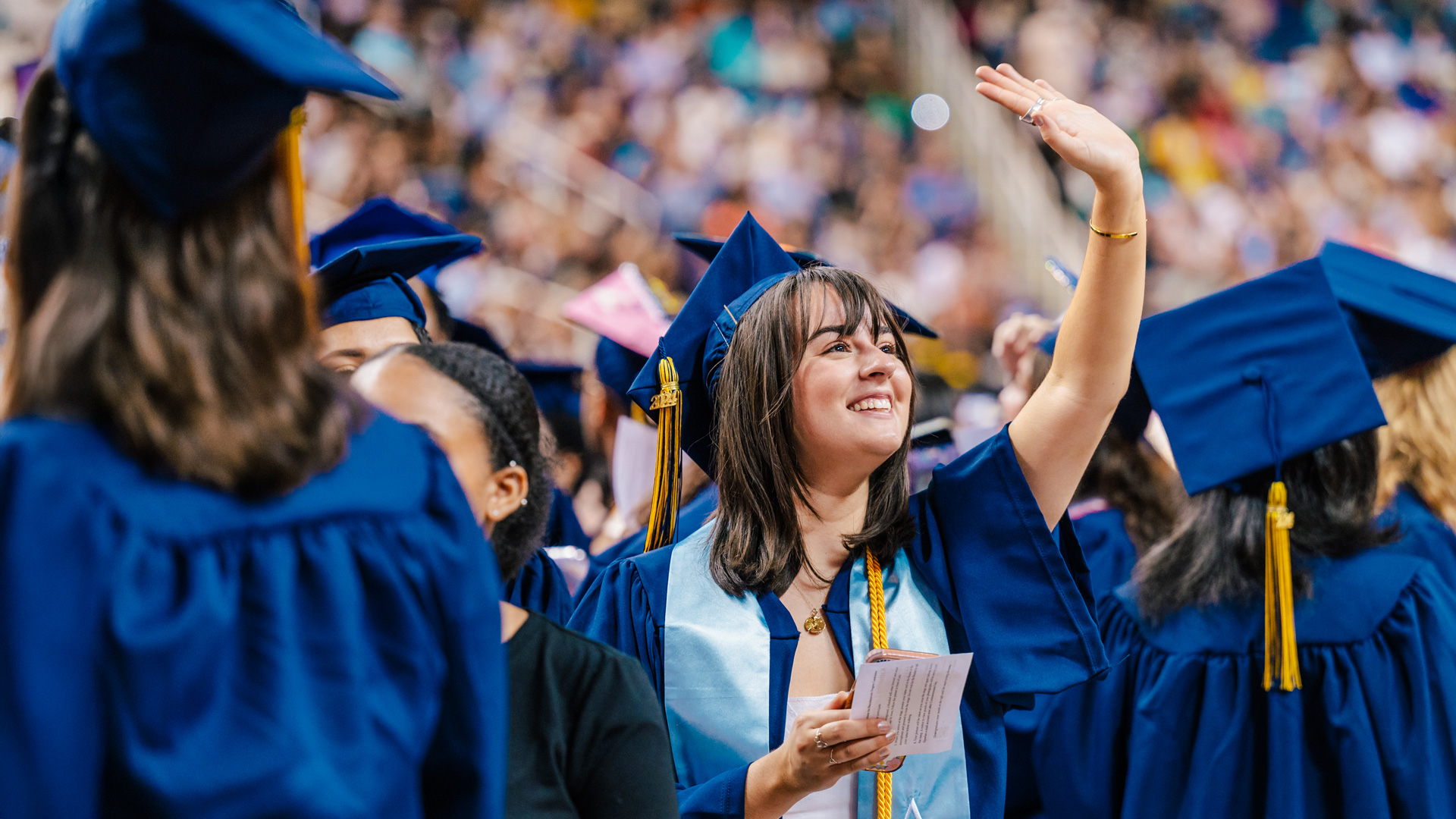 A smiling graduate waves to the crowd.