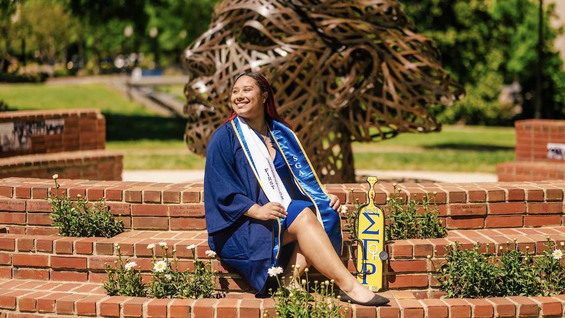 UNCG School of Nursing graduate Jyesha McKinney poses outside in front of Minerva statue.