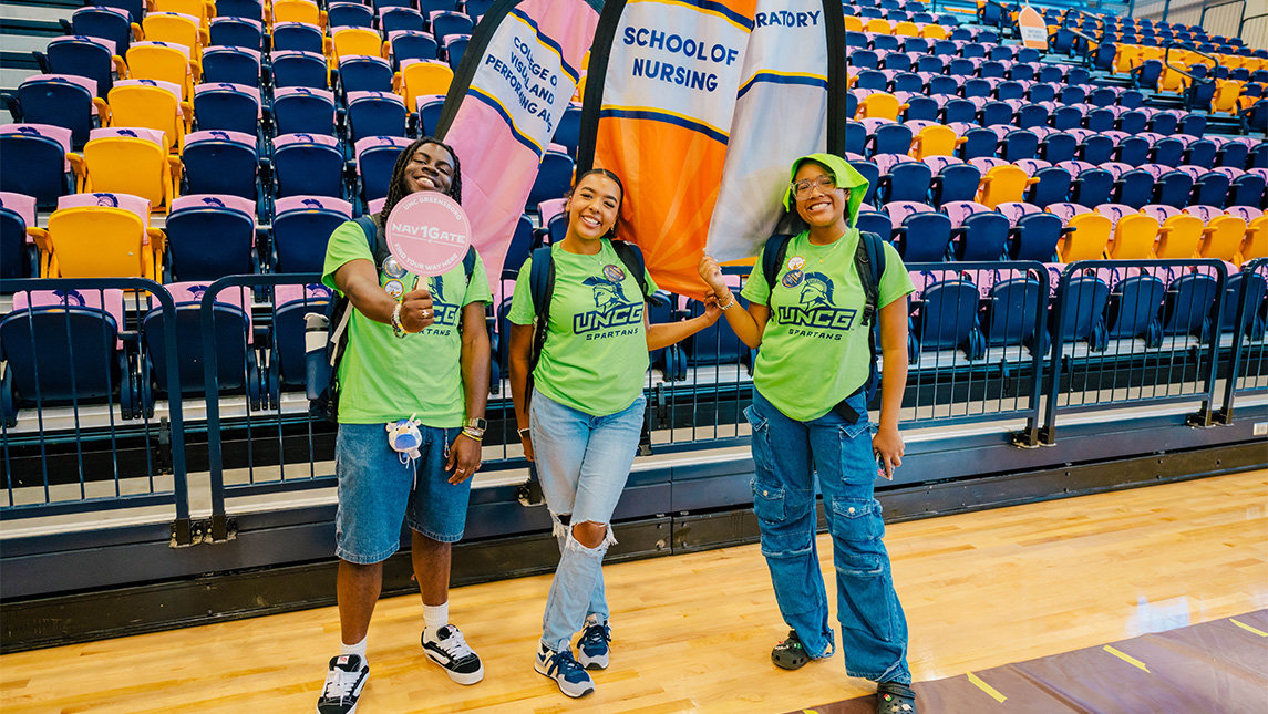 UNCG volunteers wearing green Navigate shirts and carrying flags.