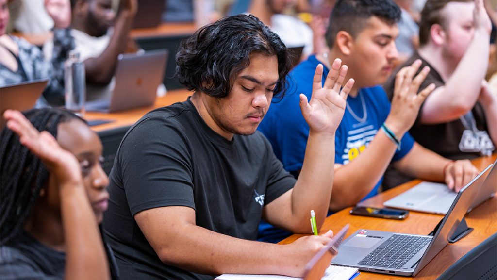 UNCG students raise their hands during class.