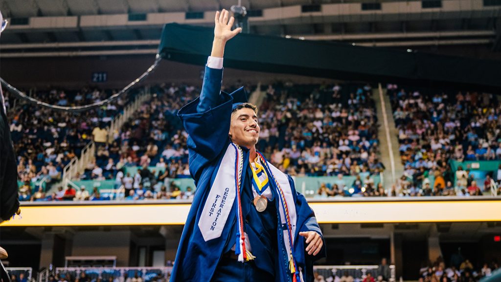 A UNCG student waves while crossing the state at Commencement.