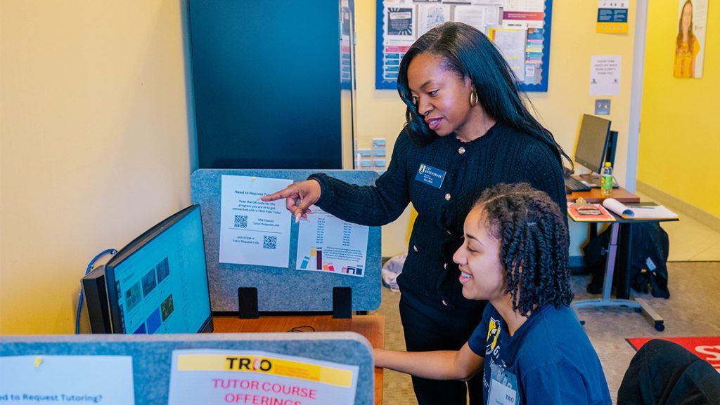 A UNCG success staffmember helps a student at a computer station.