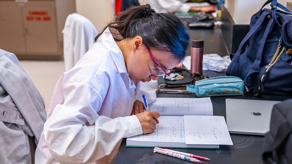 A UNCG student in a lab coat goes over her notes.