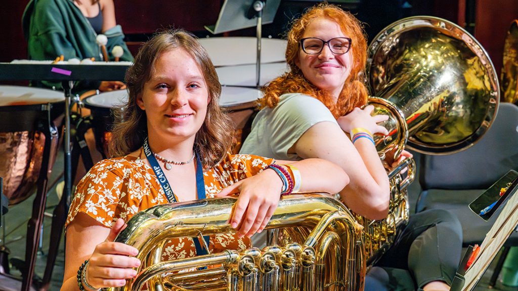 High school girls smile with their musical instruments at UNCG.