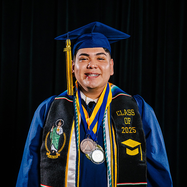 Student in cap and gown with lots of stoles, cords and medals poses with a big smile in a black studio.