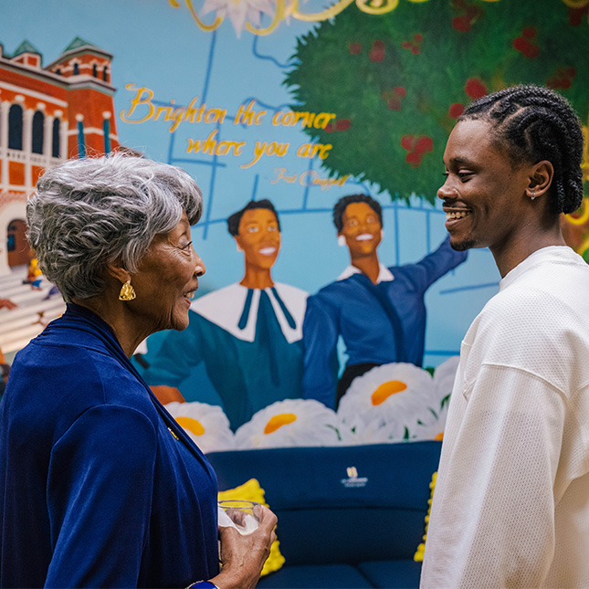 Young man talks to a older woman in front of a painted mural.