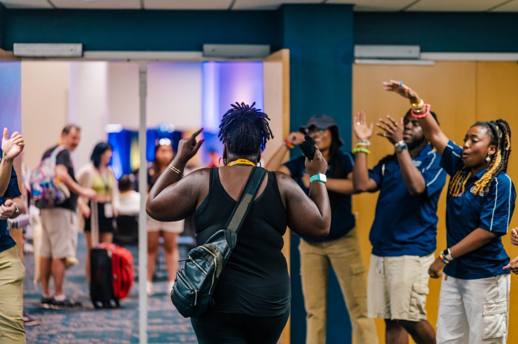 Mother of a student walks into a conference room as orientation leaders cheer her on at the doorway.