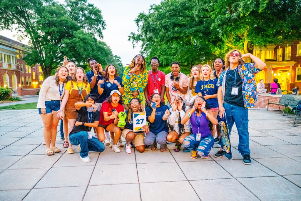 Small orientation group pose together with their leader on a campus sidewalk.