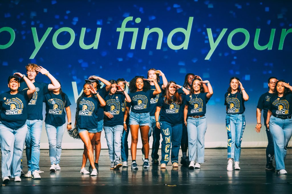 Group of students dance on stage in matching t-shirts. 