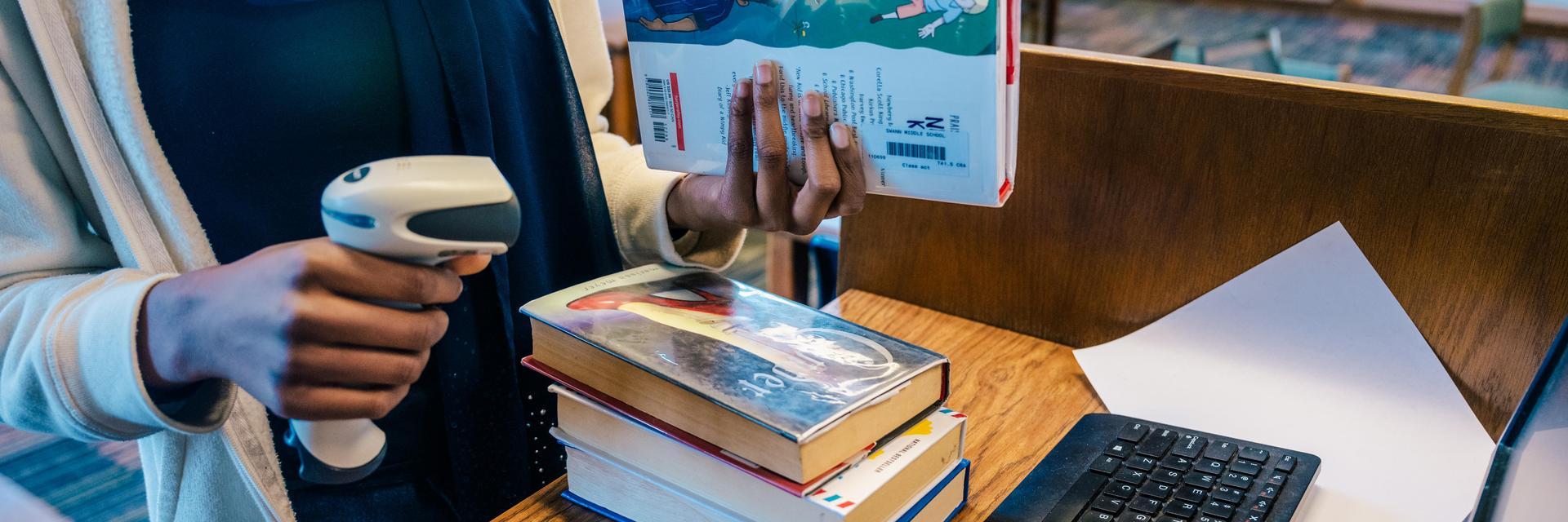 person holding a book and scanner at a computer