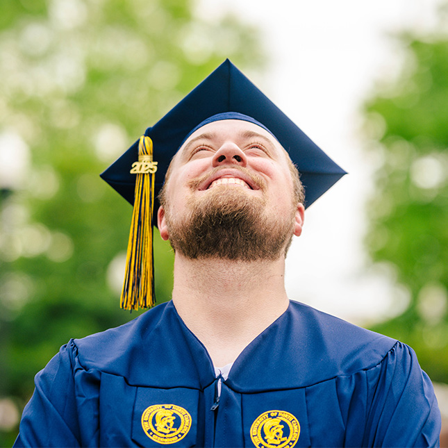 Close-up of a 2025 graduate in cap and gown as he looks up. 