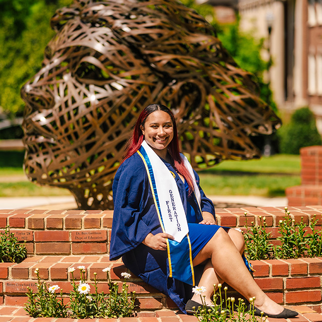 Graduate sits in front of Astera stature and shows off her First Generation stole.