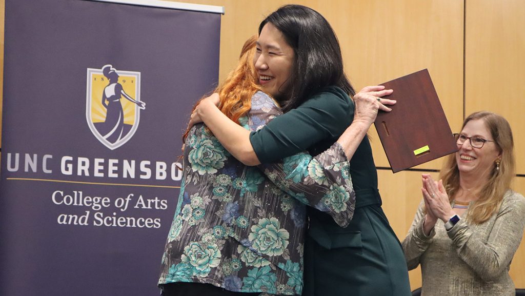 Faculty members hug during an awards ceremony for UNCG's College of Arts and Sciences.