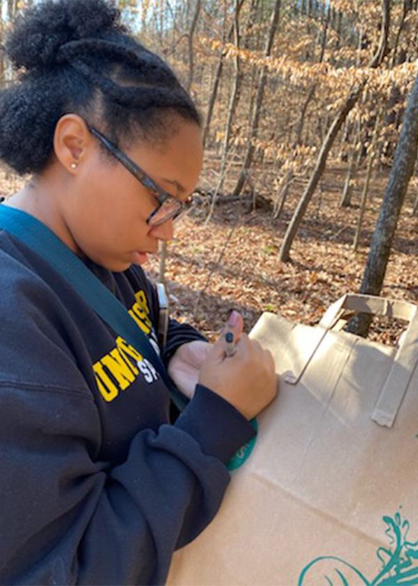 UNCG student Janae Wofford takes notes out in the woods.