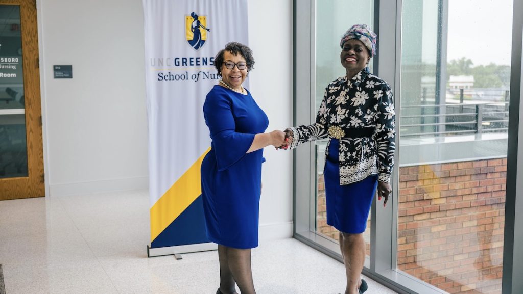 Dean Barksdale and Vivian Dennis shake hands in front of UNCG School of Nursing sign.