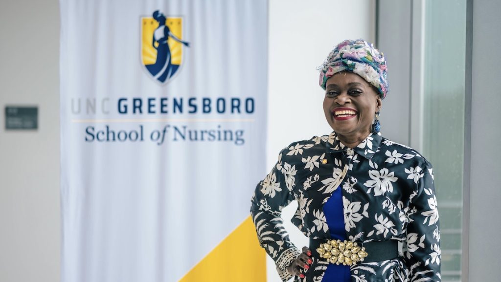 Vivian Dennis poses in front of UNCG School of Nursing sign.
