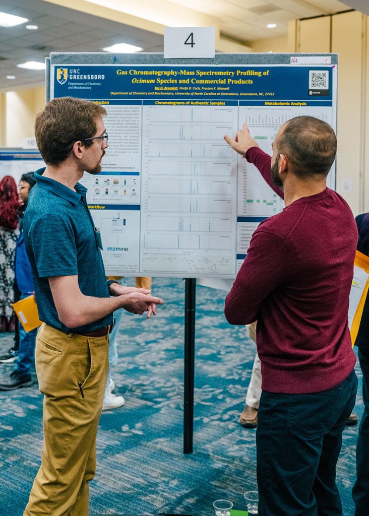 A UNCG explains his research while someone points at his poster.