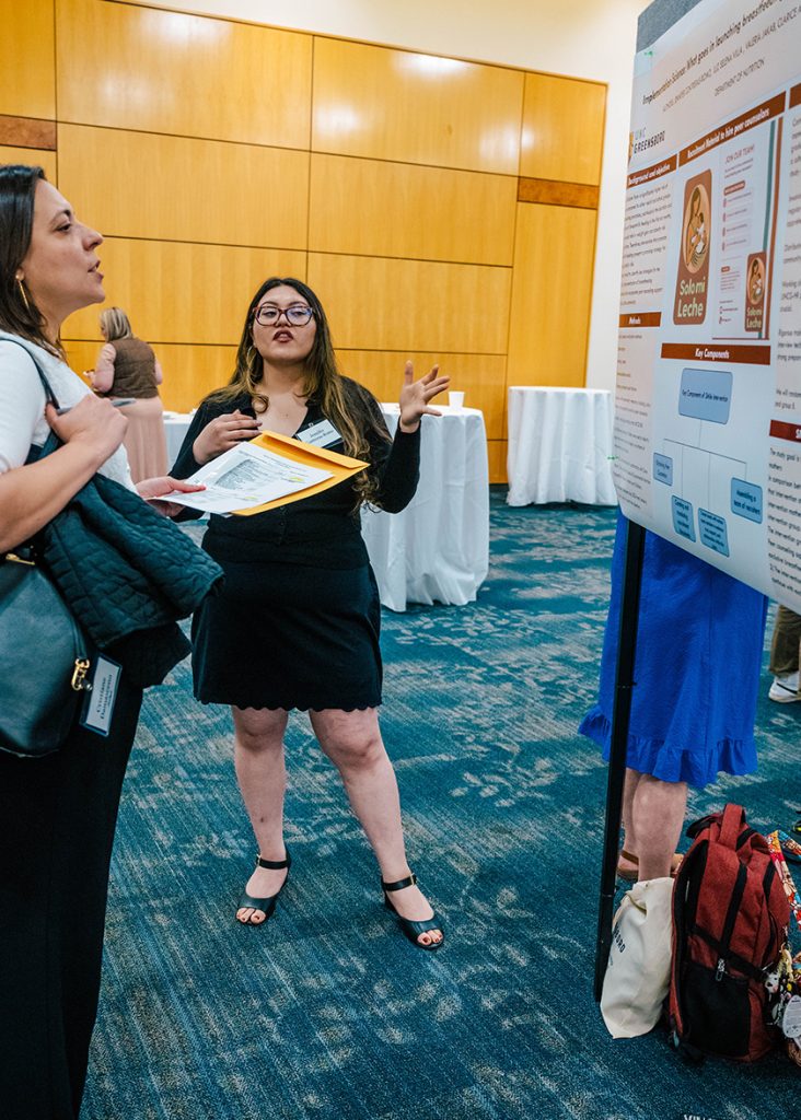 UNCG students chat next to a research poster.