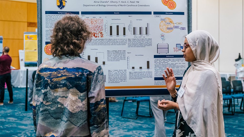 A UNCG student explains a research posterboard.