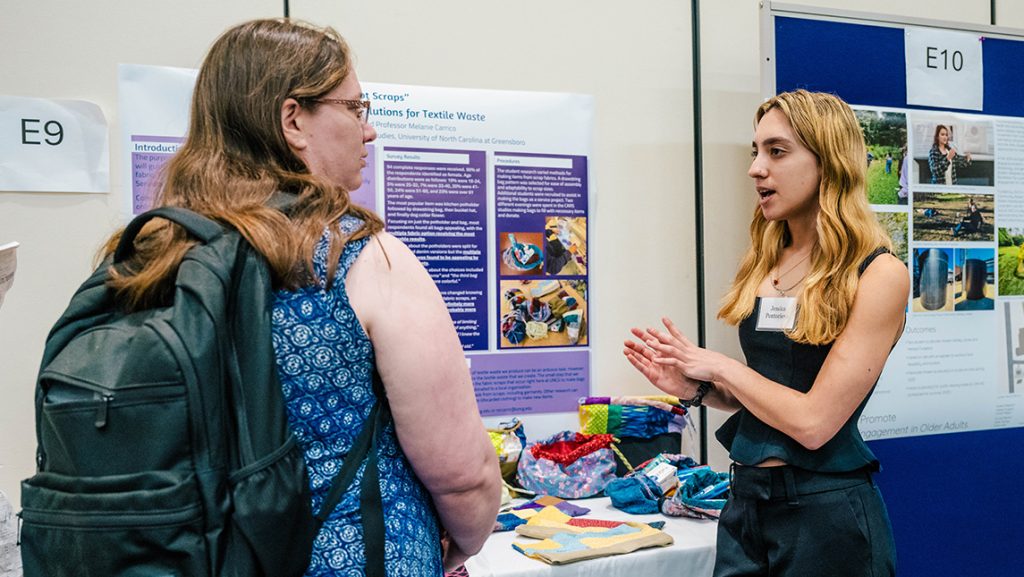 A UNCG student shows fabric samples on display.
