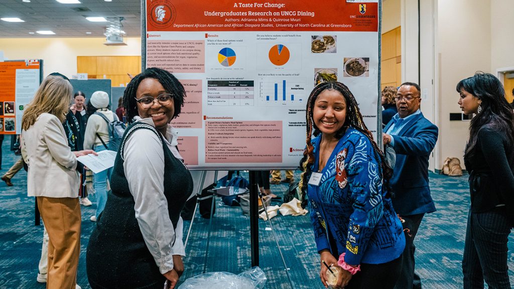 UNCG students Quinrose Mvuri and Adrianna Mims pose next to their research poster.