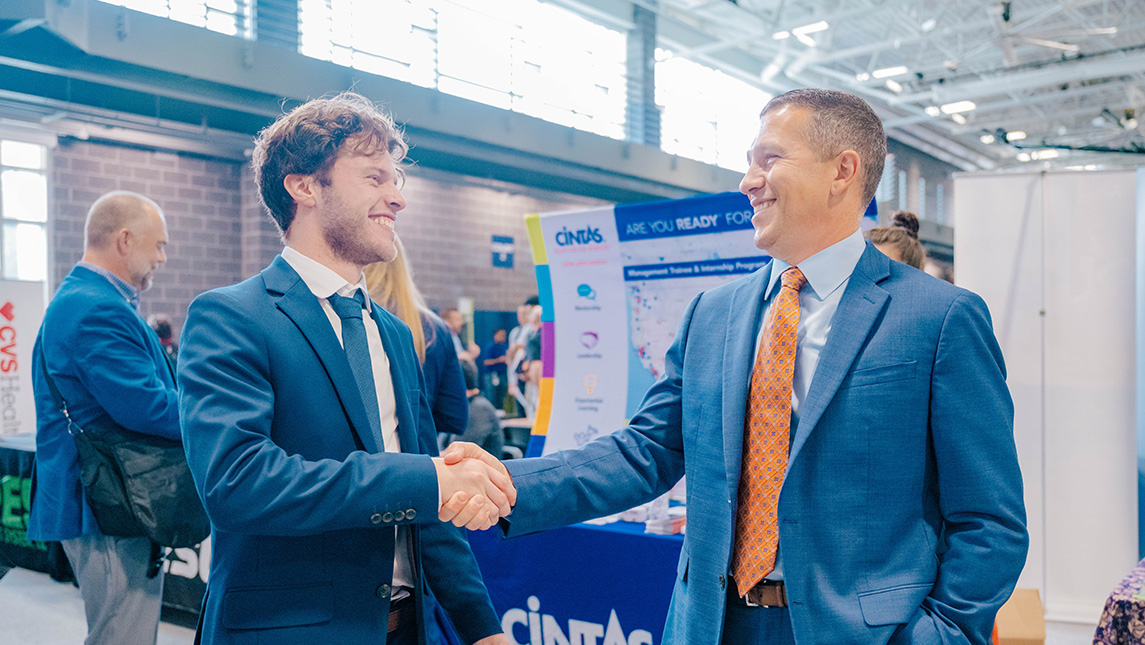 Two men shake hands at a career fair.