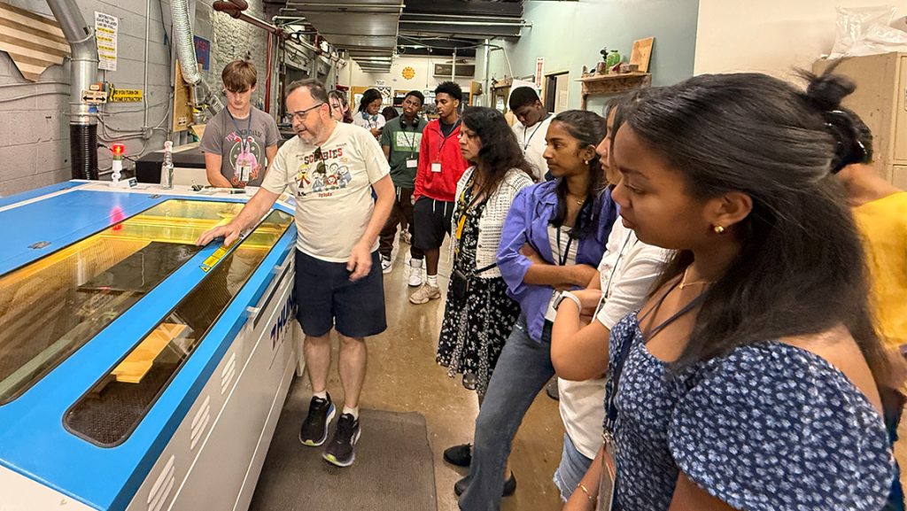 Students look at a glass engraving machine at Forge Greensboro.