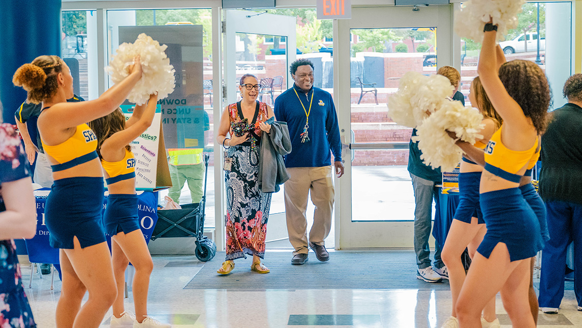 UNCG cheerleaders wave pom-poms at faculty and staff.
