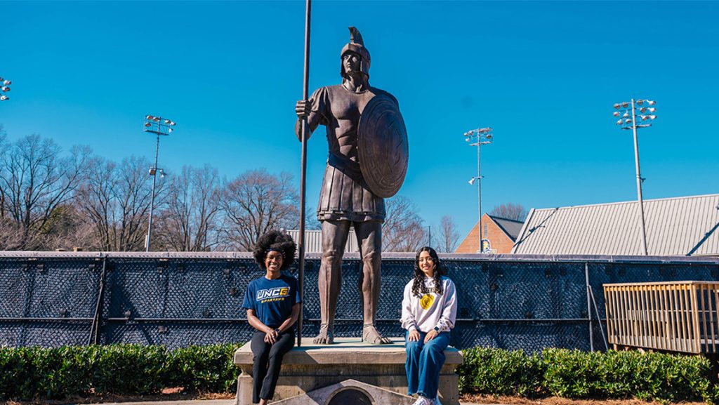 UNCG students pose next to Spartan statue.